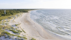 A beach with a lighthouse, sandy shore, and ocean waves. - View Luksusowy Apartament SPA Ko Obrzeg Polanki Aqua (Kołobrzeg)