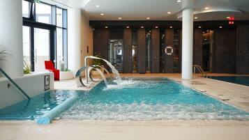 An indoor swimming pool with a water feature, surrounded by a modern interior with large windows and a seating area.