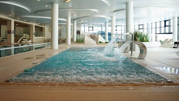 A large indoor swimming pool with a waterfall feature, surrounded by a spacious lobby with high ceilings and modern architecture. - View Luksusowy Apartament SPA Ko Obrzeg Polanki Aqua (Kołobrzeg)