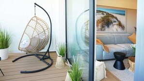 A modern living room with a hanging chair, a sofa, and a large window with a beach view. - View Luksusowy Apartament SPA Ko Obrzeg Polanki Aqua (Kołobrzeg)