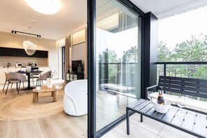 A modern living room with a glass wall, a dining area with a round table, and a balcony with a bench. - Sunrise Tw j Prywatny Widok na Ba tyk (Trzebiatow)