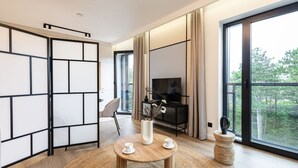 A modern living room with a large sliding glass door leading to a balcony, a flat-screen TV, a wooden coffee table with cups, and a vase with dried branches. - Sunrise Tw j Prywatny Widok na Ba tyk (Trzebiatow)
