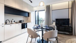 A modern kitchen with white cabinets, a dining area with a round table, and a flat-screen TV. - Sunrise Tw j Prywatny Widok na Ba tyk (Trzebiatow)