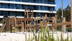 A playground with wooden structures and a building with multiple floors in the background. - Sereno Apartament Blisko pla y Widok na Natur (Trzebiatow)