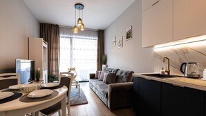 A modern kitchen with a central island, a dining area with a table set for two, and a living area with a sofa and a TV. - Sereno Apartament Blisko pla y Widok na Natur (Trzebiatow)