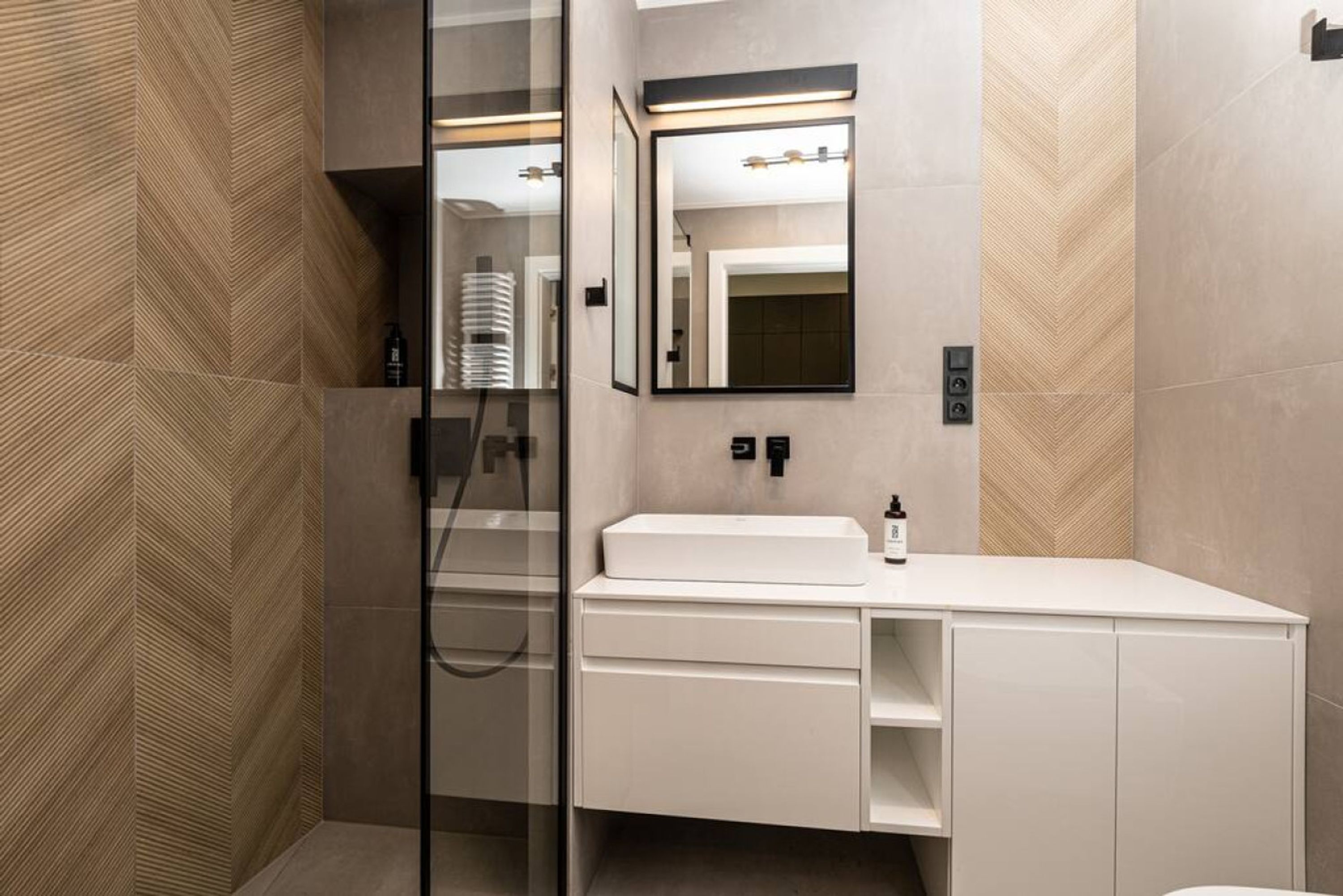 Un baño moderno con cabina de ducha de vidrio, tocador blanco y un espejo grande con iluminación integrada.