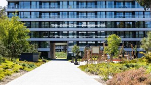 A modern multi-story building with a central entrance, surrounded by landscaped gardens and outdoor seating areas. - Patio Shellter Komfort Mi dzy Morzem a Jeziorem (Trzebiatow)