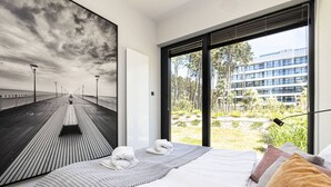 A modern hotel room with a large bed, a view of a wooden pier, and a building in the background. - Patio Shellter Komfort Mi dzy Morzem a Jeziorem (Trzebiatow)