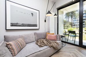 A modern living room with a grey sofa, a framed black and white photograph, and a glass door leading to an outdoor area. - Patio Shellter Komfort Mi dzy Morzem a Jeziorem (Trzebiatow)