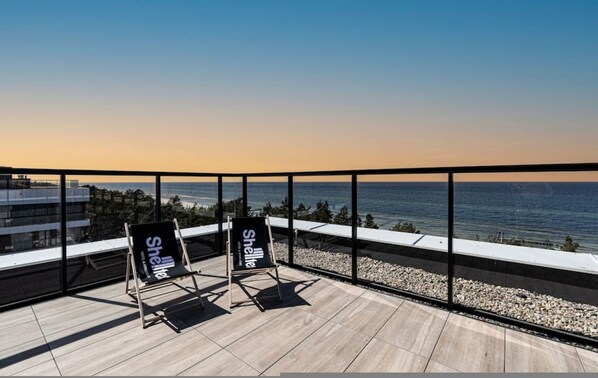 A rooftop terrace with a view of the ocean, featuring two chairs with 'Shelter' branding. - Patio Shellter Komfort Mi dzy Morzem a Jeziorem (Trzebiatow)