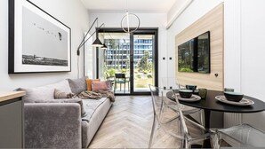 A modern living room with a sofa, a dining table with chairs, a large window, and a framed picture on the wall. - Patio Shellter Komfort Mi dzy Morzem a Jeziorem (Trzebiatow)