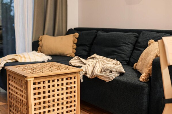 A dark-colored sofa with multiple cushions, a woven basket, and a striped blanket. - Loco Stylowy Mokot w Szybki Dojazd do Centrum (Warsaw)