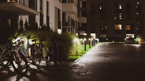 Ein Nachtbild eines Mehrfamilienhauses mit Balkonen, einem gepflasterten Gehweg und abgestellten Fahrrädern.