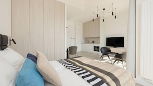 A modern bedroom with a large bed, a TV, a desk, and a kitchenette. - Art Forrest 33 M in Rogowo (Trzebiatow)