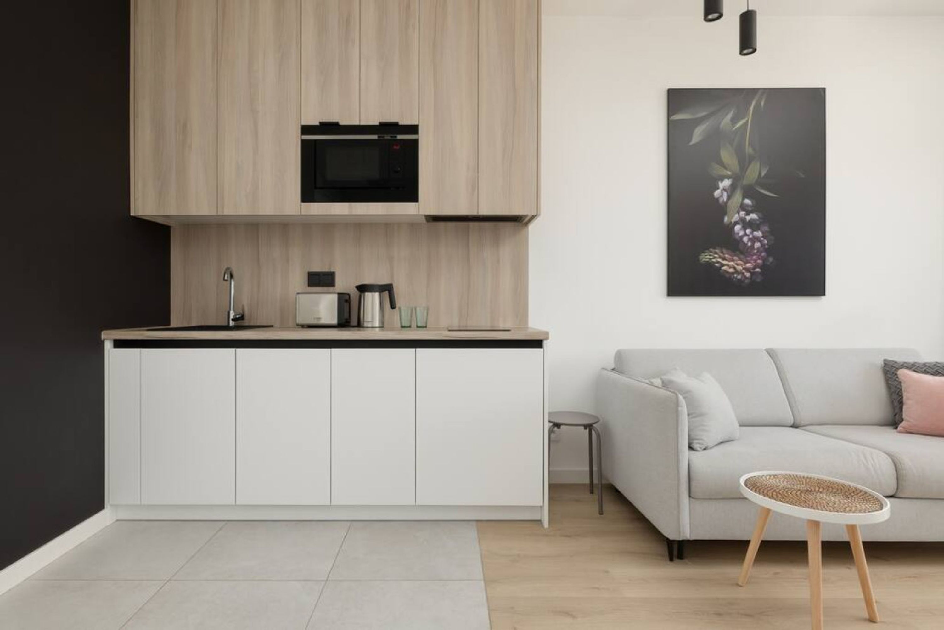 Una cocina moderna con microondas integrado, cafetera y una pequeña isla. En la zona de estar, hay un sofá gris y una mesa de mimbre.