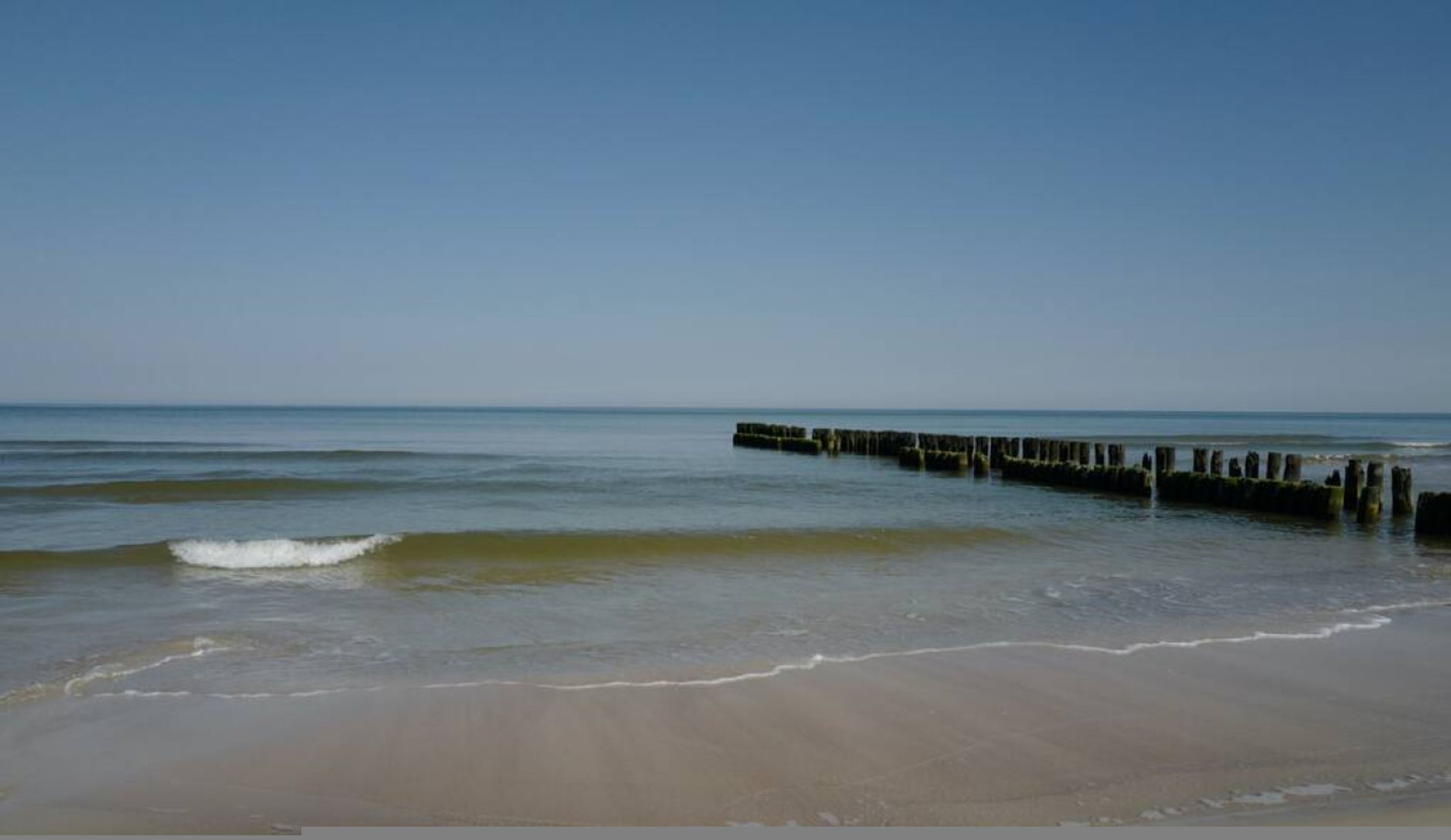 A beach with a wooden pier extending into calm waters.