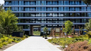 A modern multi-story building with a central entrance, surrounded by greenery and a paved walkway. - Art Forrest 33 B in Rogowo (Trzebiatow)