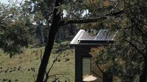 Eine moderne Holzhütte mit Solardach, umgeben von Bäumen und einer grasbewachsenen Hügelsicht.