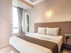 Una habitación de hotel moderna con una cama grande, una mesita de noche con lámpara y una ventana con cortinas.