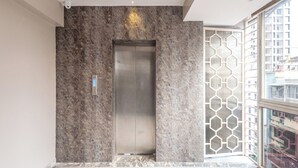 Un elevador moderno con detalles metálicos, una pared con textura y una puerta de diseño geométrico.