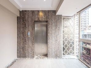 Un elevador moderno con detalles metálicos, una pared con textura y una puerta de diseño geométrico.