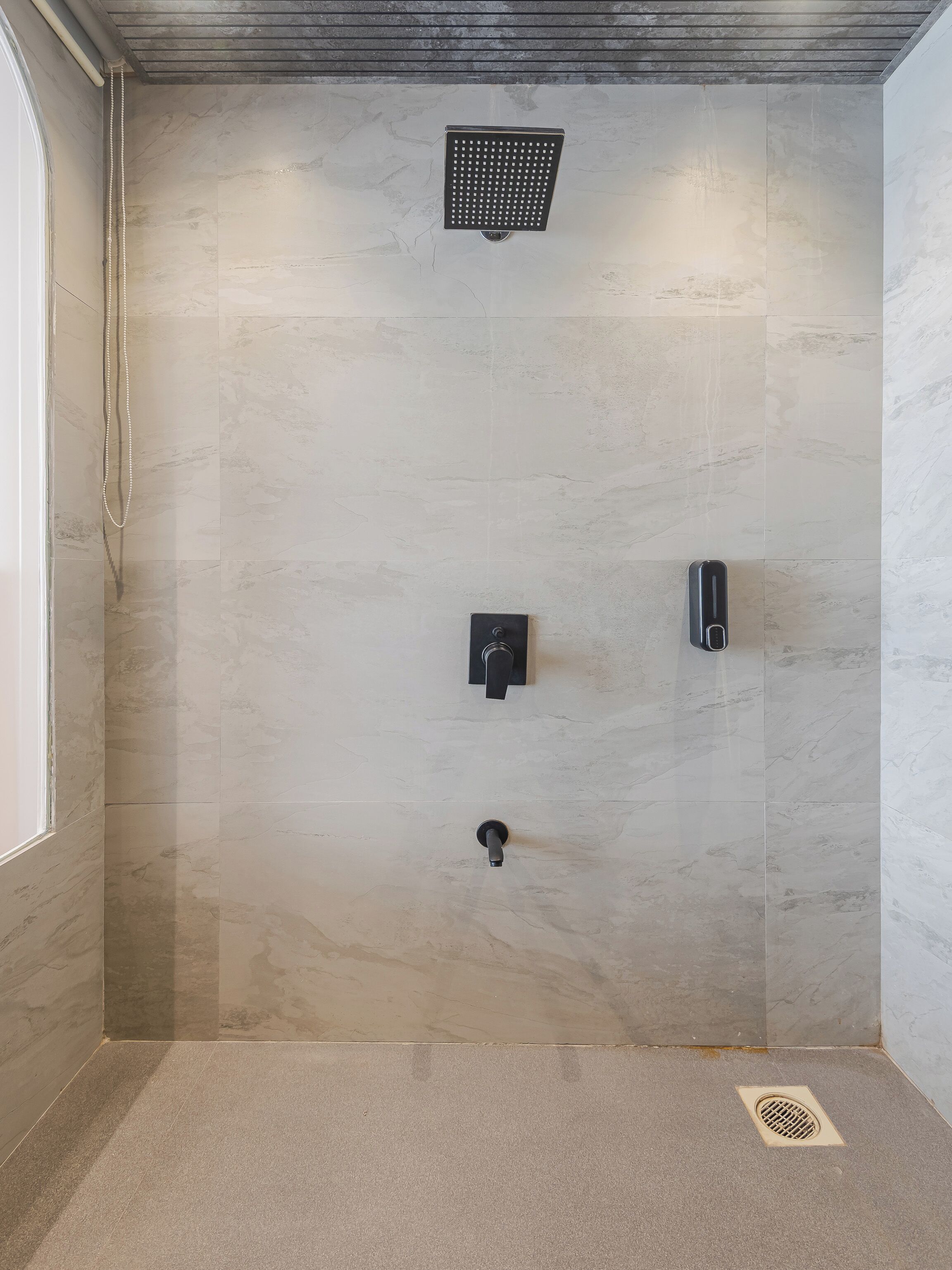 Un espace douche avec un mur en marbre, une douchette à main et un panneau de commande fixé au mur.