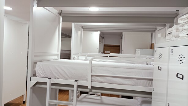 A bunk bed room with white bedding, a wooden floor, and a white wardrobe with a mirror. - ALBERGUE VALIN LAMA (Palas de Rei)