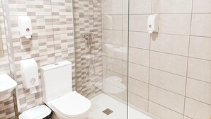 A modern bathroom with a toilet, a shower with a glass door, and hand soap dispensers. - ALBERGUE VALIN LAMA (Palas de Rei)