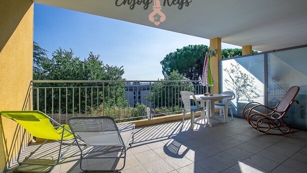En balkon med udsigt til bygninger og træer, et bord med stole, og et skilt der siger "Enjoy Keys".