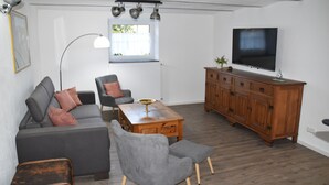 Un salon avec un canapé gris, un fauteuil gris, une table basse en bois, un téléviseur posé sur un meuble en bois et un lampadaire.