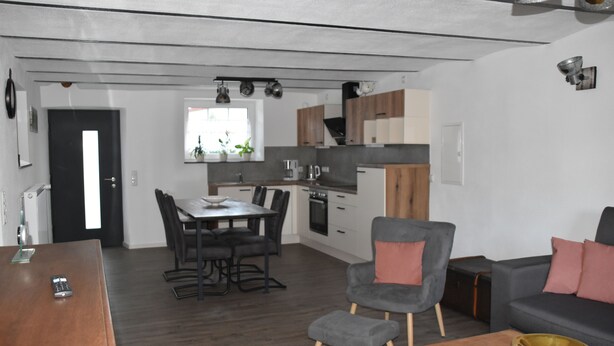 Une cuisine moderne avec un coin repas, un canapé gris et une table basse en bois.