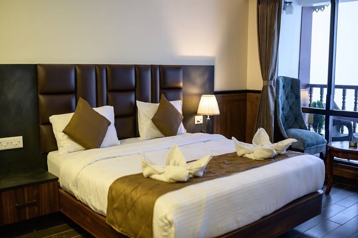 A hotel room with a large bed, dark wood headboard, and a view of the outdoors through a window.