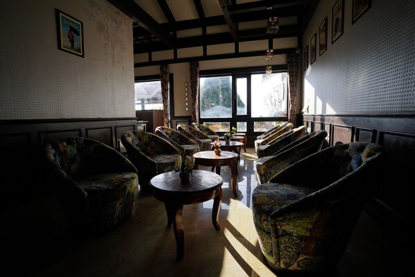 A spacious lobby with patterned armchairs, a central round table with a vase, and large windows offering a view of the outdoors.