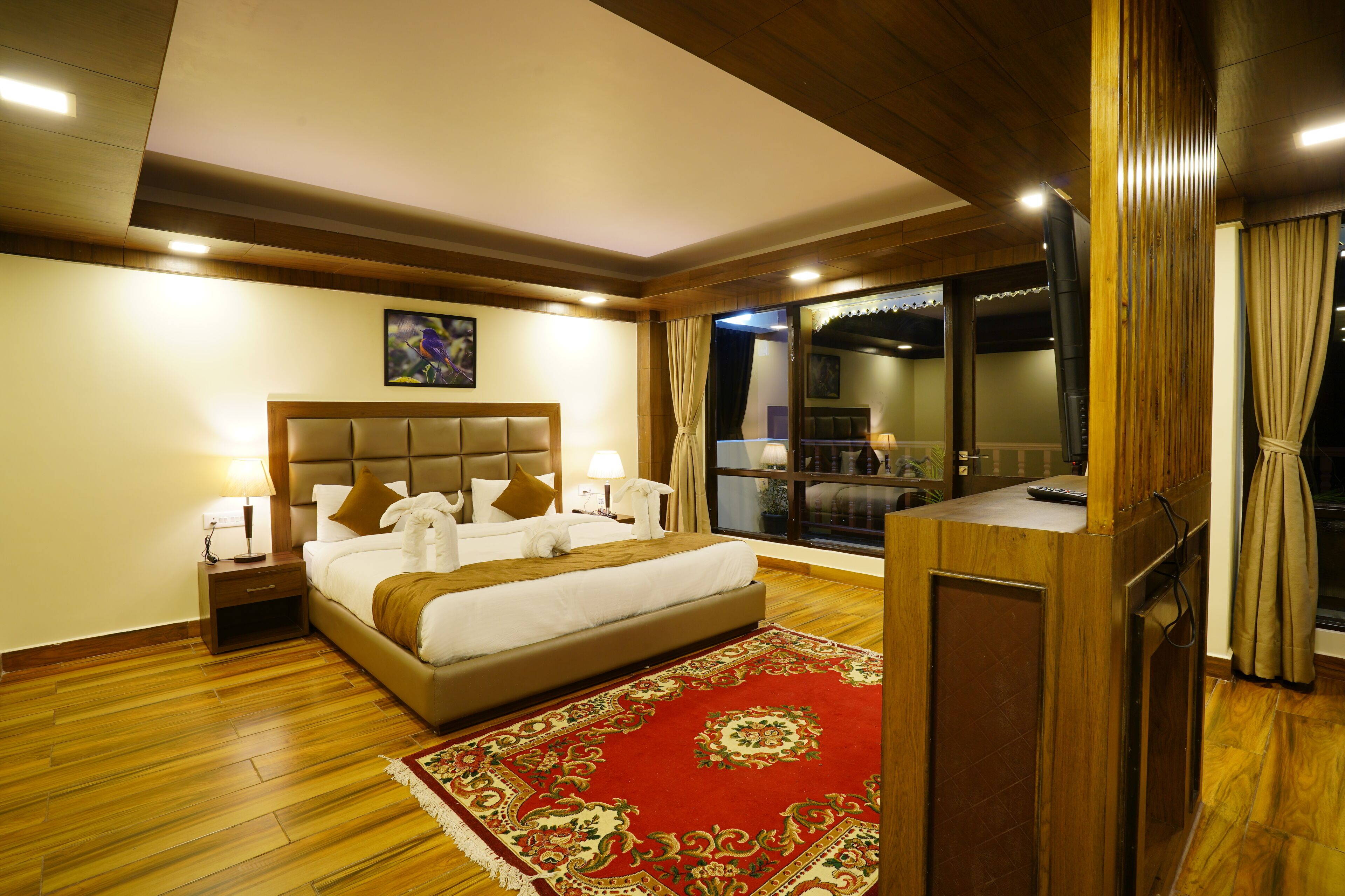 A hotel room with a large bed, wooden flooring, a red carpet, and a view of the outside.