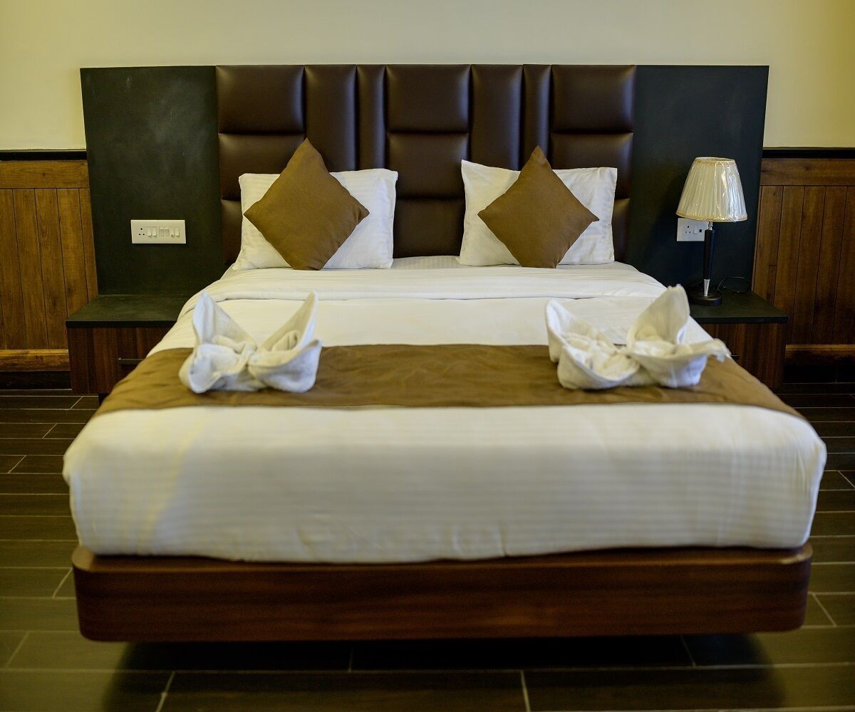 A neatly made bed with a brown headboard, white bedding, and two brown pillows.
