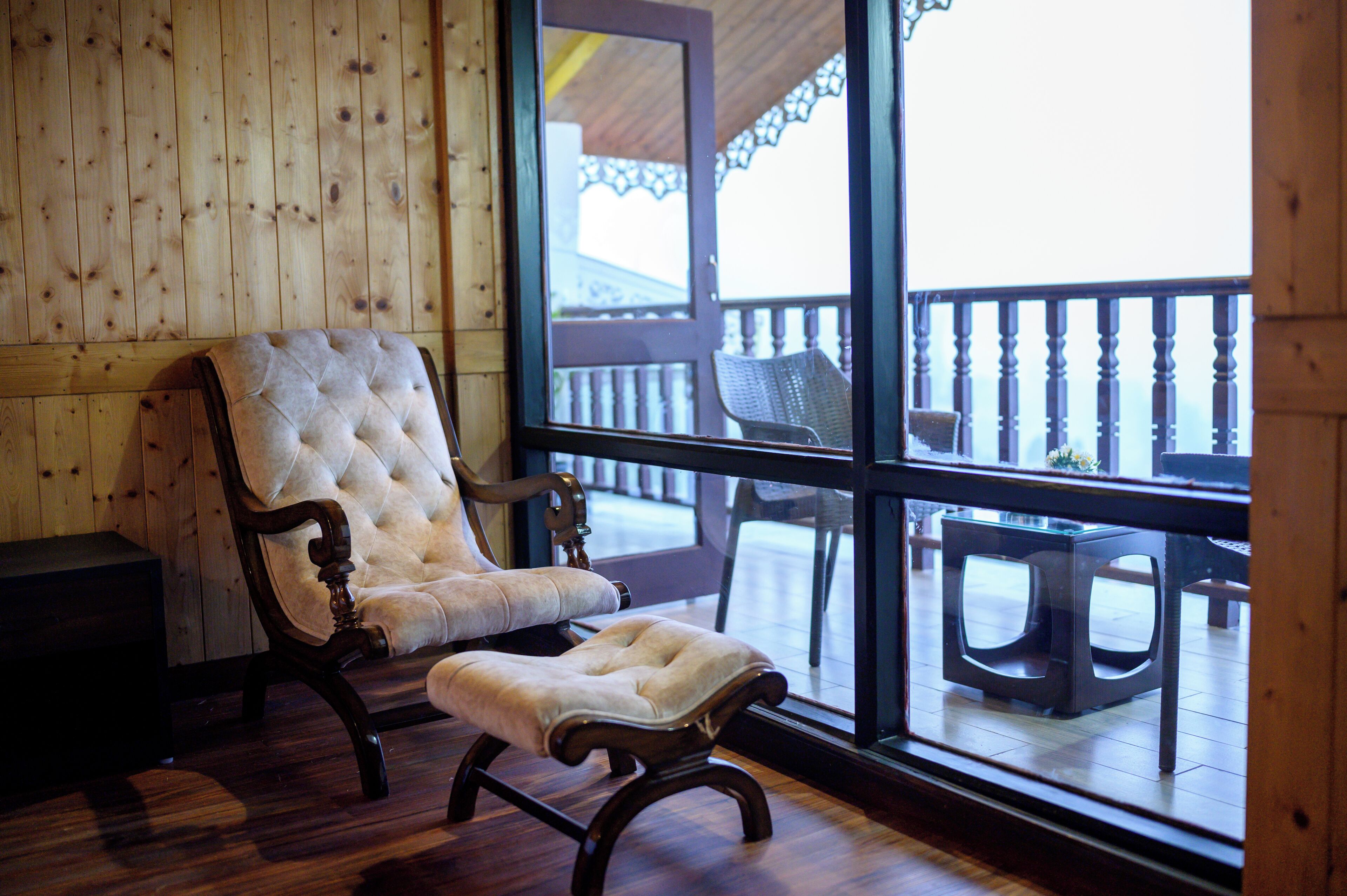 Un interior de madera con un ventanal grande, un sillón capitonado y un reposapiés a juego.