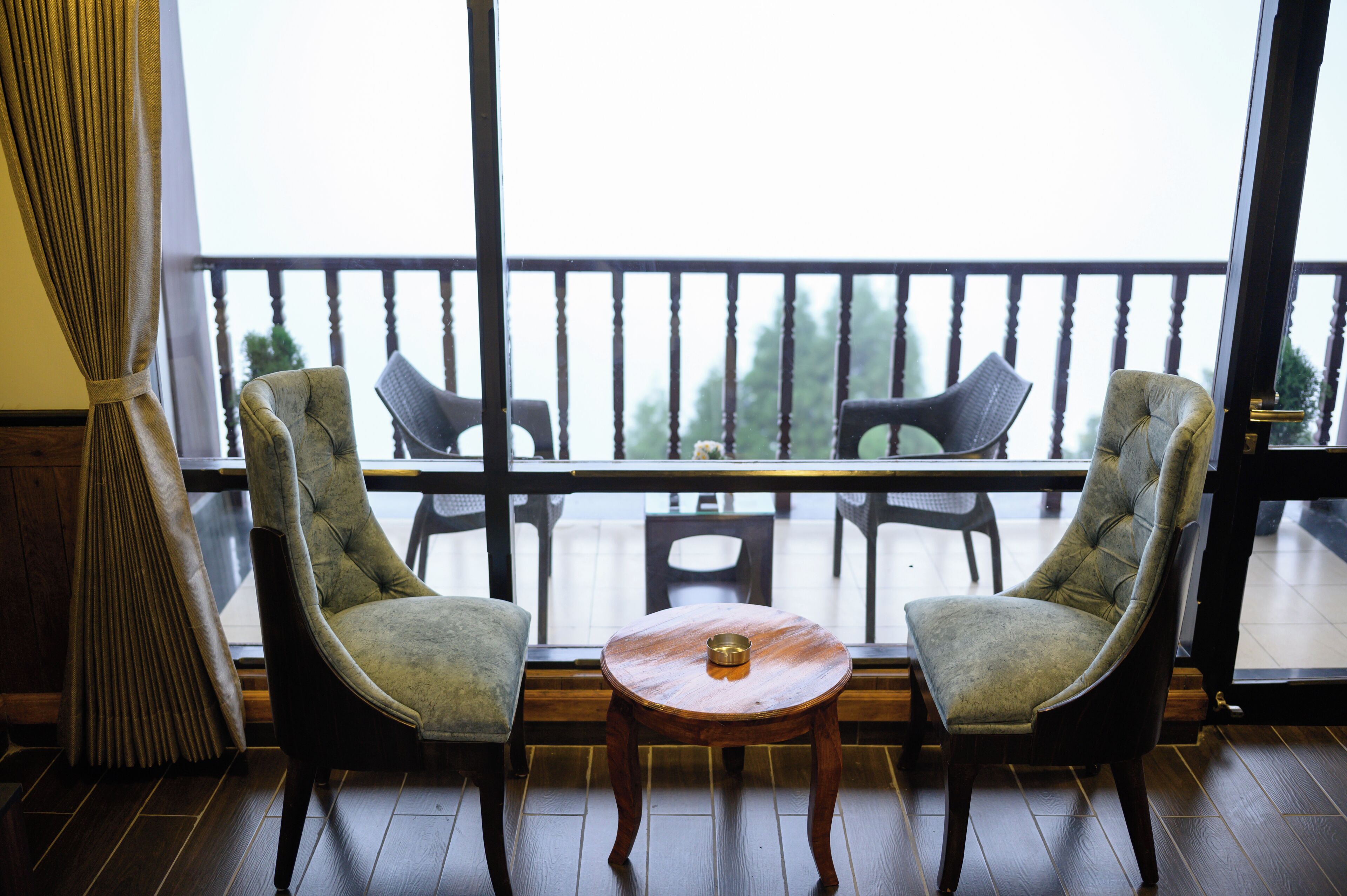 Un balcón con dos sillones tapizados, una mesita redonda y vistas al exterior.