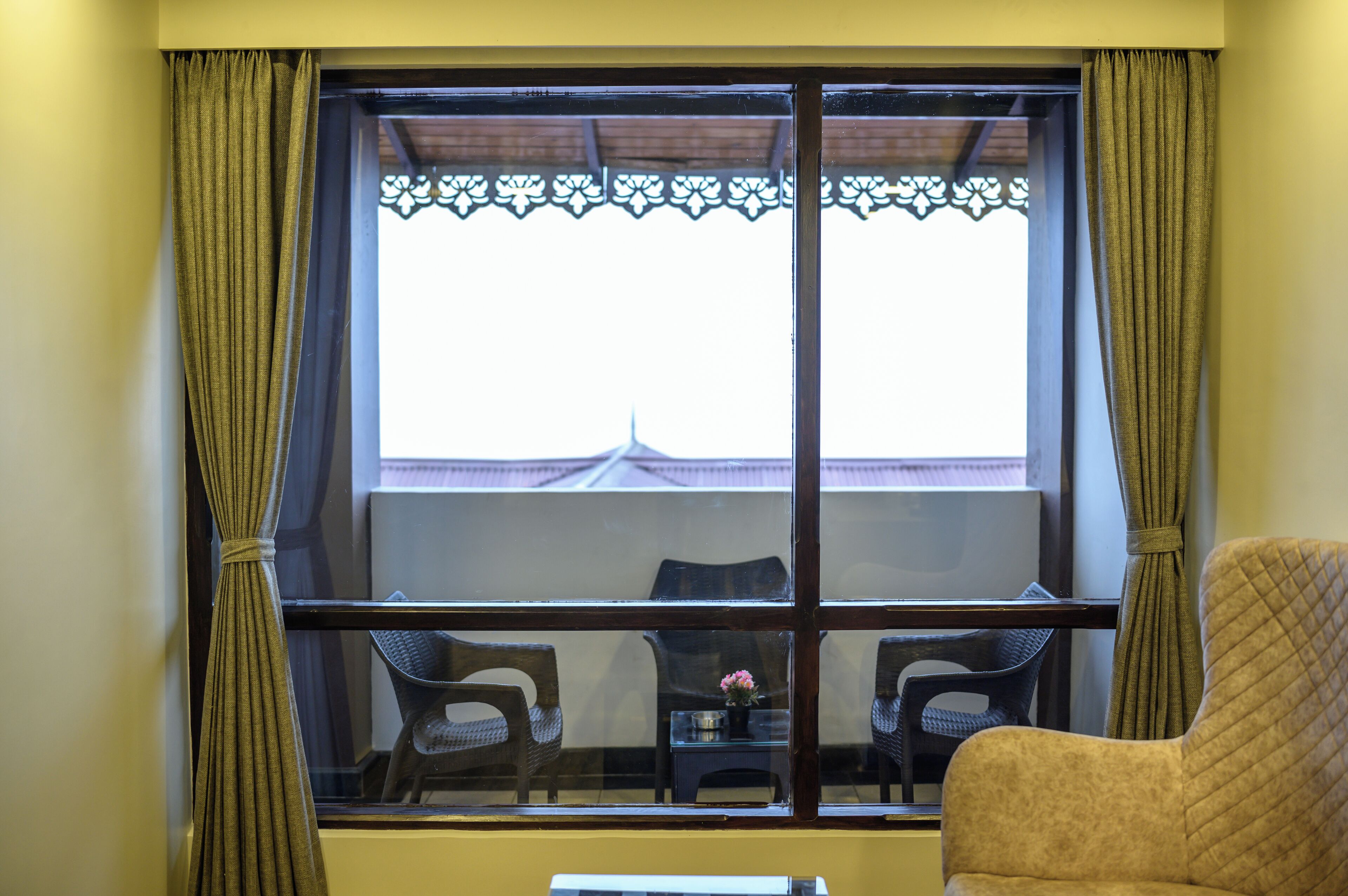 A room with a large window, two chairs, and a small table with a flower vase.