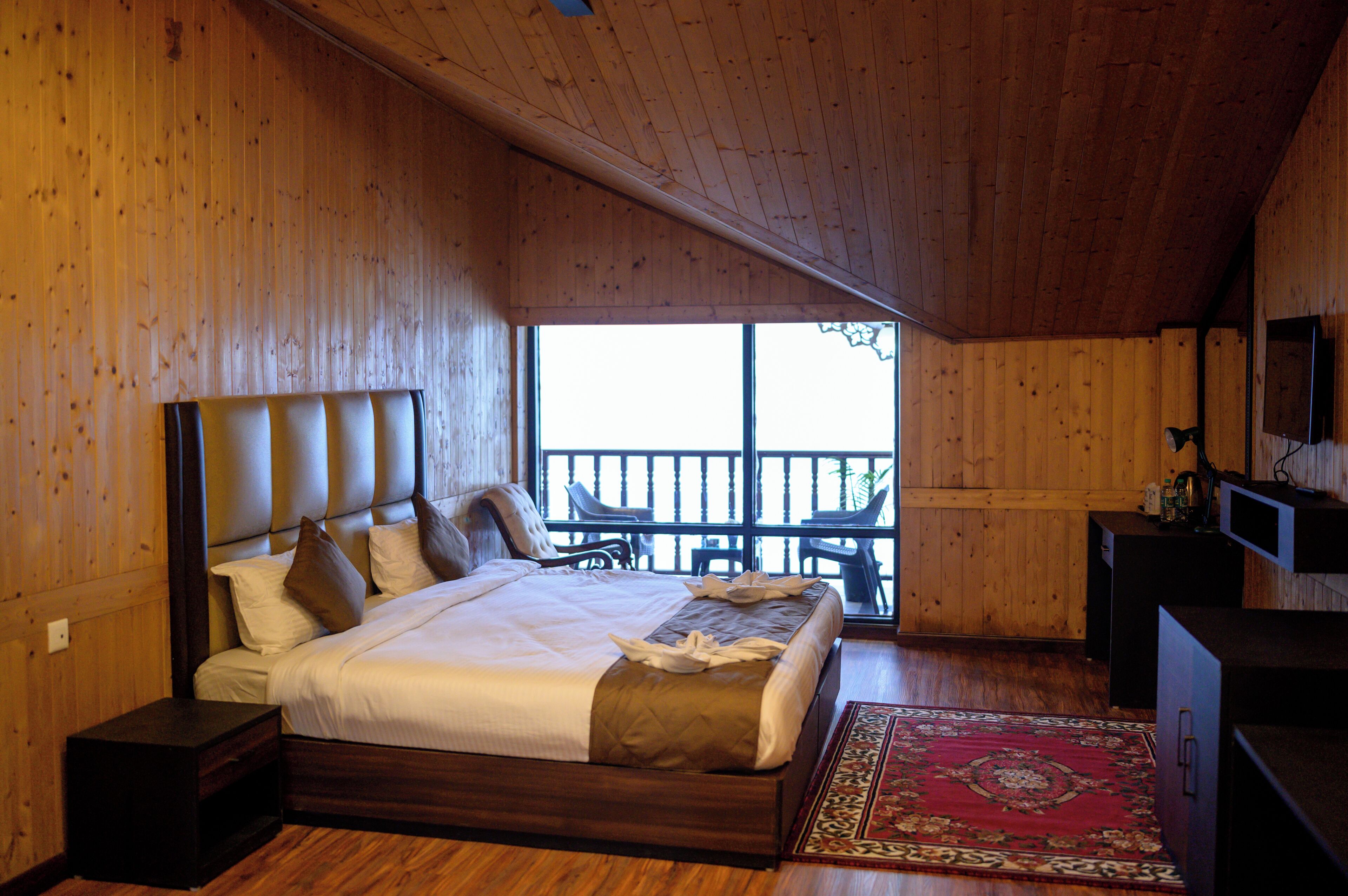 Ein Schlafzimmer mit Holzwänden, einem großen Bett, einem Fernseher und einem Balkon mit Sitzgelegenheiten.
