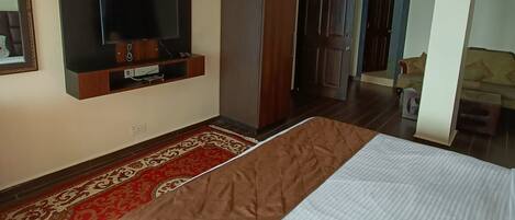 A hotel room with a bed, a television mounted on the wall, a wardrobe, and a door leading to another room.