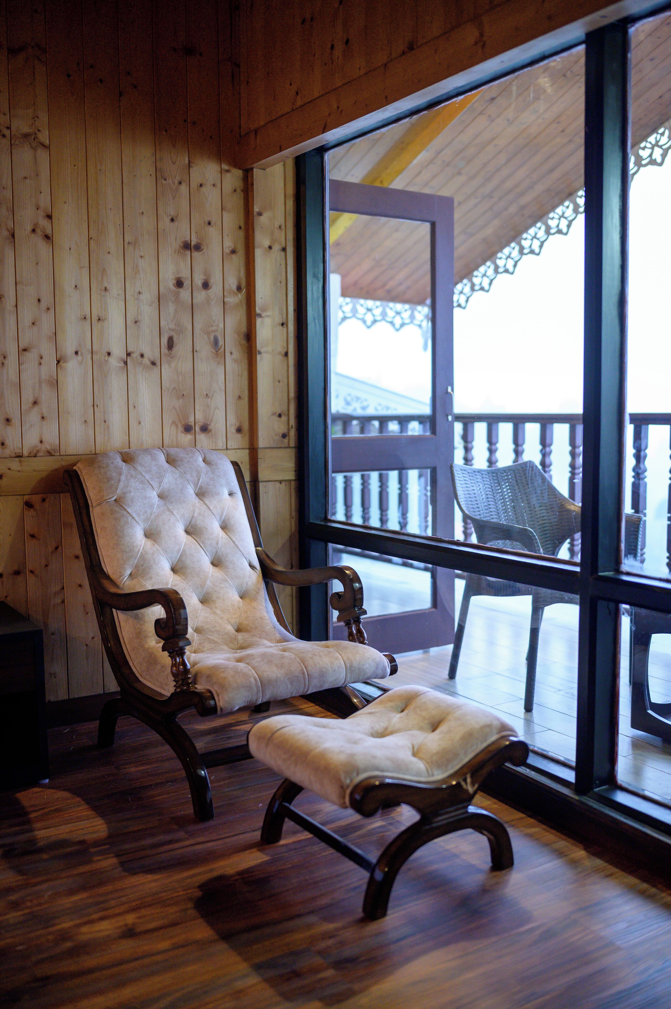 A wooden-paneled room with a large window, a tufted armchair, and a wooden bench.