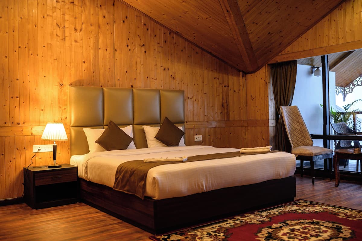 A wooden-paneled bedroom with a large bed, a nightstand, a chair, and a view of the outdoors.