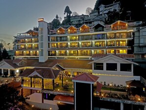 A multi-story hotel with balconies and a central tower, surrounded by smaller buildings and a landscaped area.