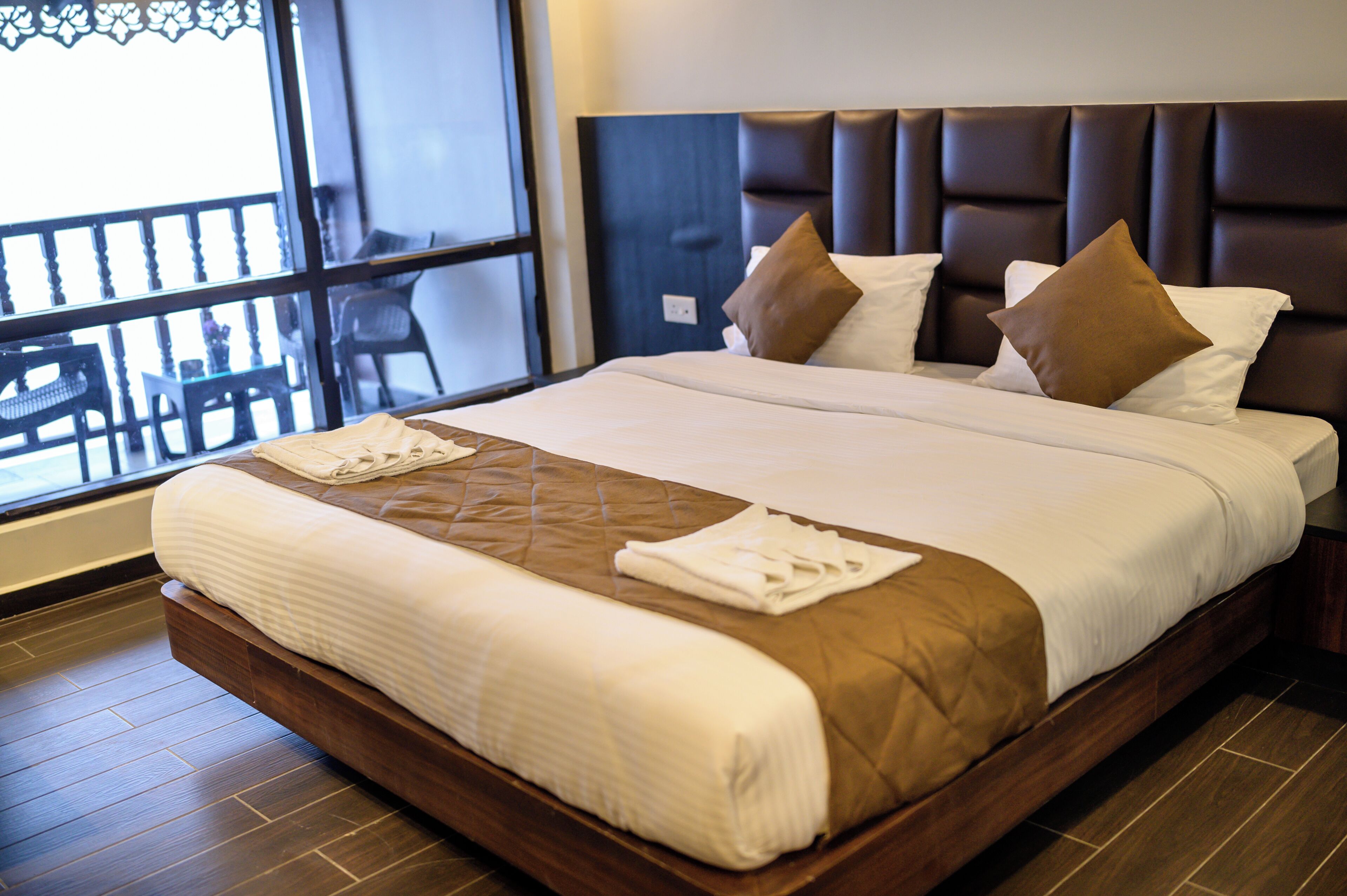 Habitación de hotel con una cama grande, cabecero y vistas al balcón exterior.
