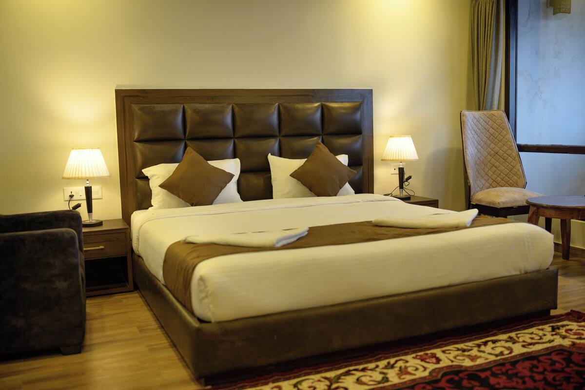 A hotel room with a large bed, two bedside tables with lamps, a chair, and a window with curtains.