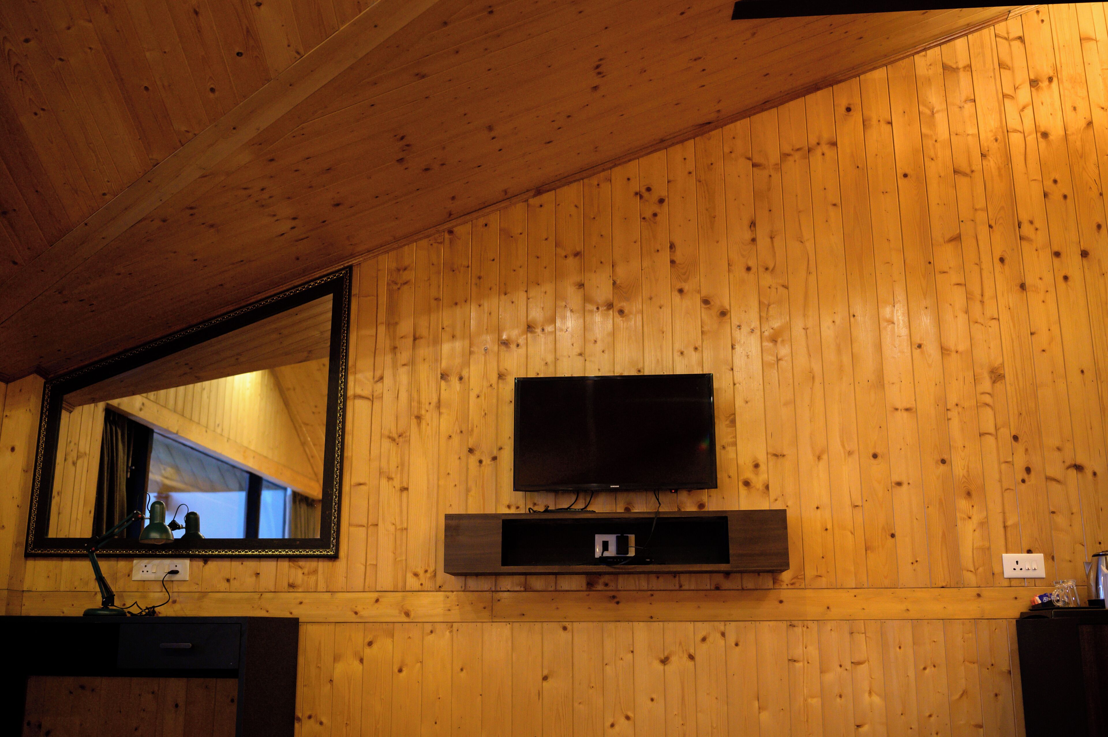 Ein Zimmer mit Holzwänden, einem an der Wand befestigten Flachbildfernseher, einem Spiegel über einem Holzkasten und einer Steckdose an der Wand.