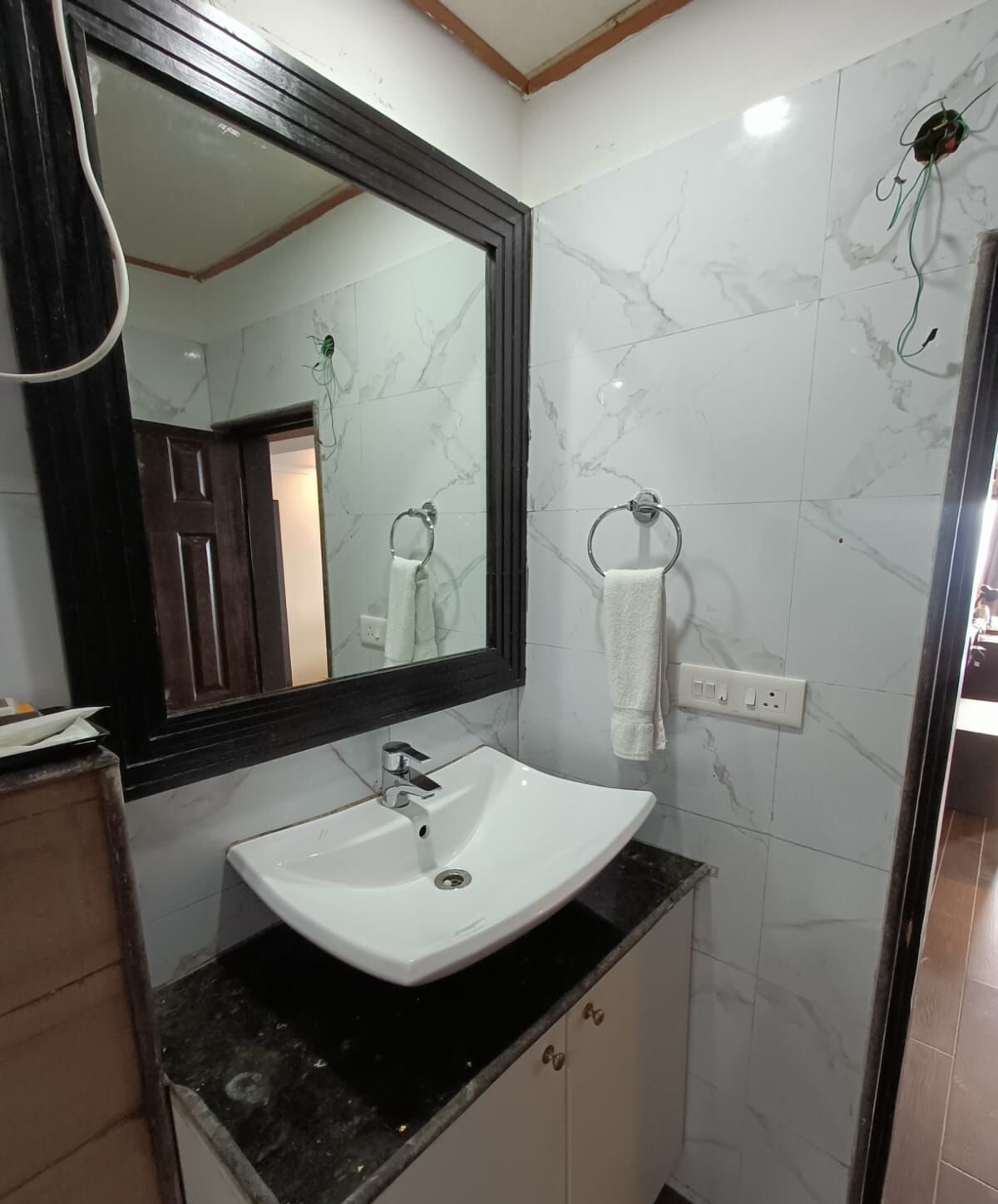 Une salle de bain avec un lavabo blanc, un grand miroir et des murs en marbre.