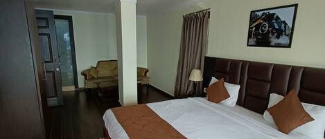 Habitación de hotel con una cama grande, un tapete rojo estampado, un armario de madera y una puerta que da a otra habitación.