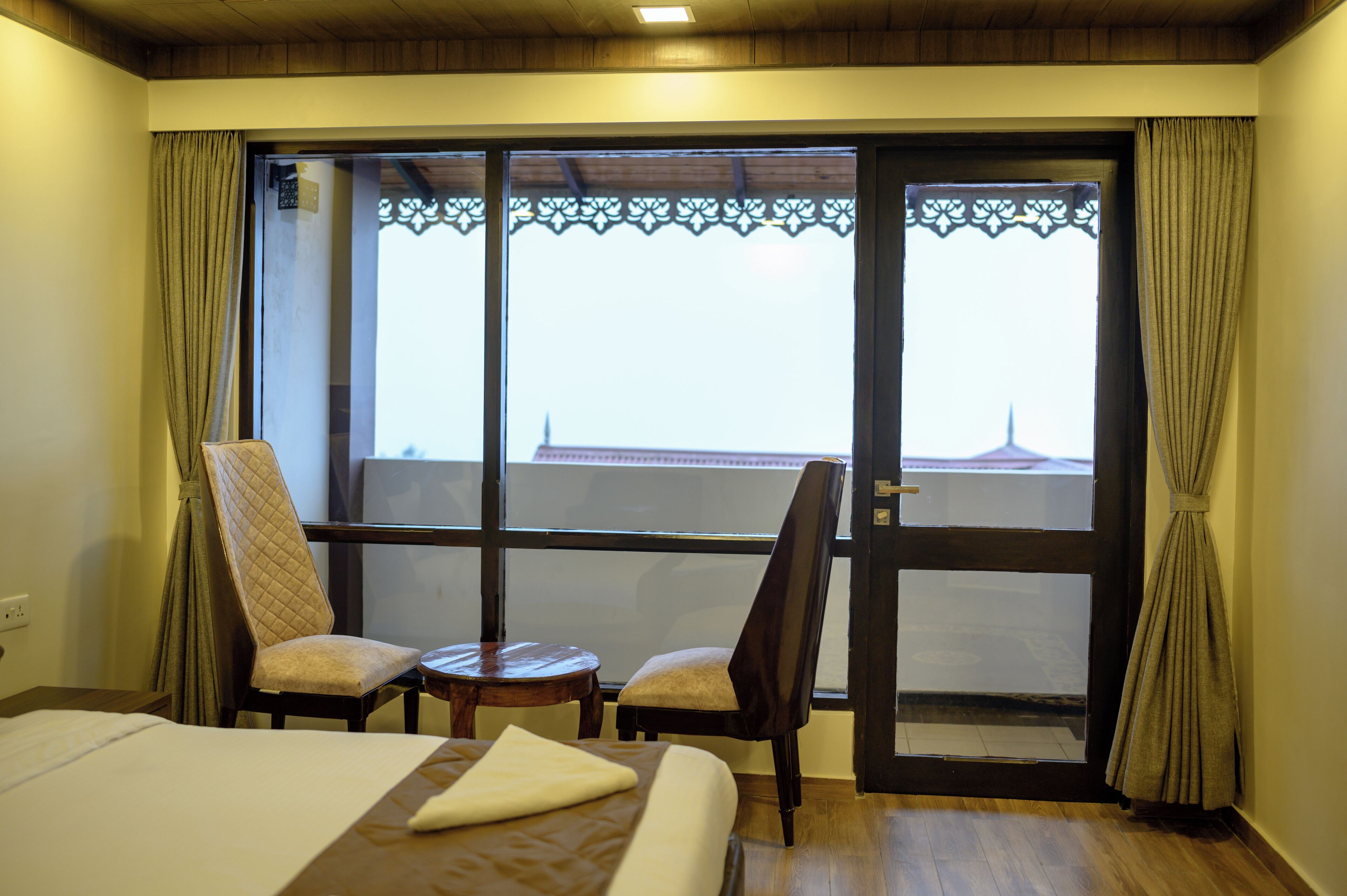 A hotel room with a bed, two chairs, a small table, and a large window with a view of a building.