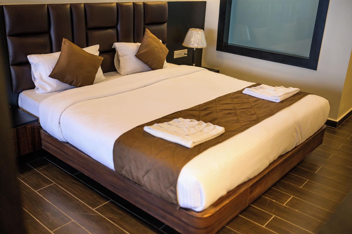 A neatly made bed with a brown headboard, white linens, and a folded towel on the bed.